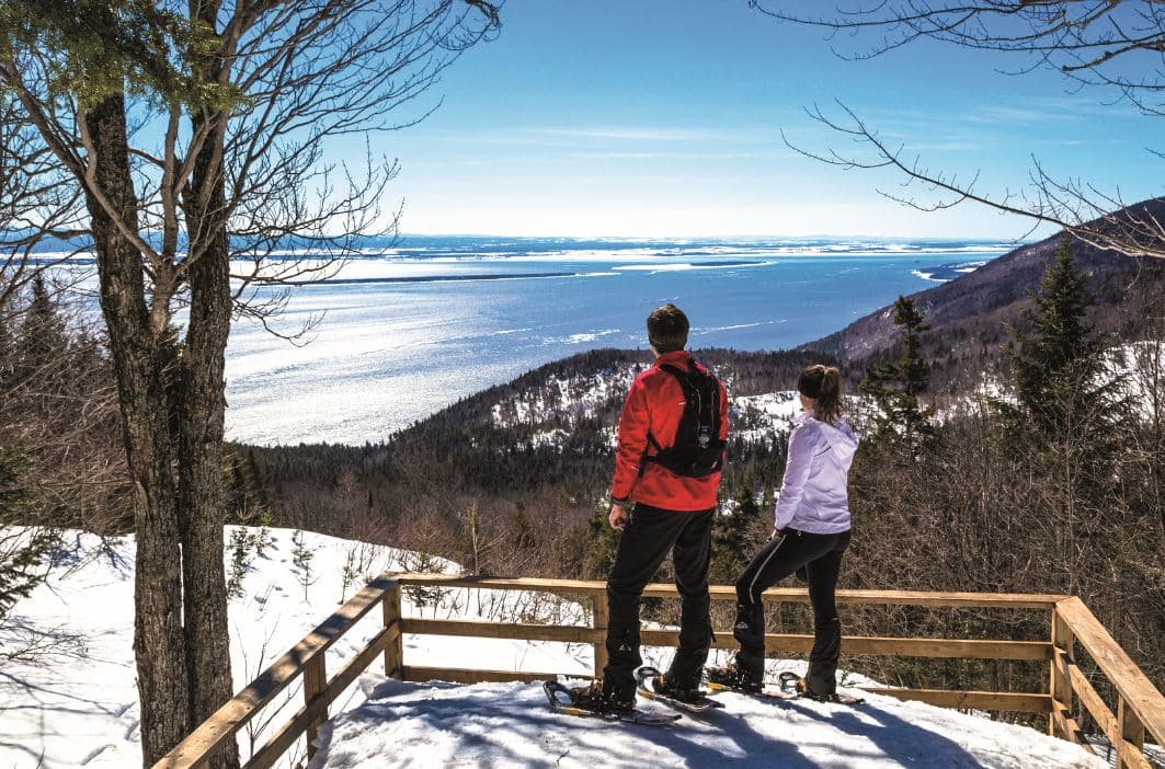 © Claude Fortin : Deux randonneurs observant la vue sur la mer depuis le sentier enneigé des Caps de Charlevoix