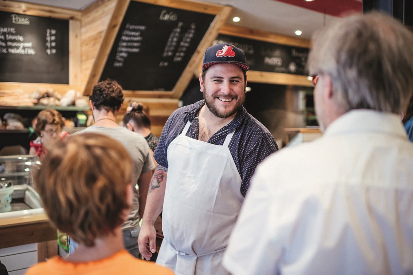 © Crémy Patisserie - Aurélie Bellacicco : un employé du restaurant accueillant de façon souriante des clients à l'intérieur de la structure